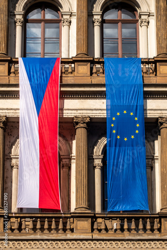 Photography Closeup front view of a Czech flag next to a EU flag hanging on a balcony  on a old city building in Prague