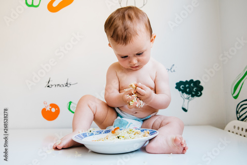 Baby taking handfuls of food to put in his mouth and eat them.