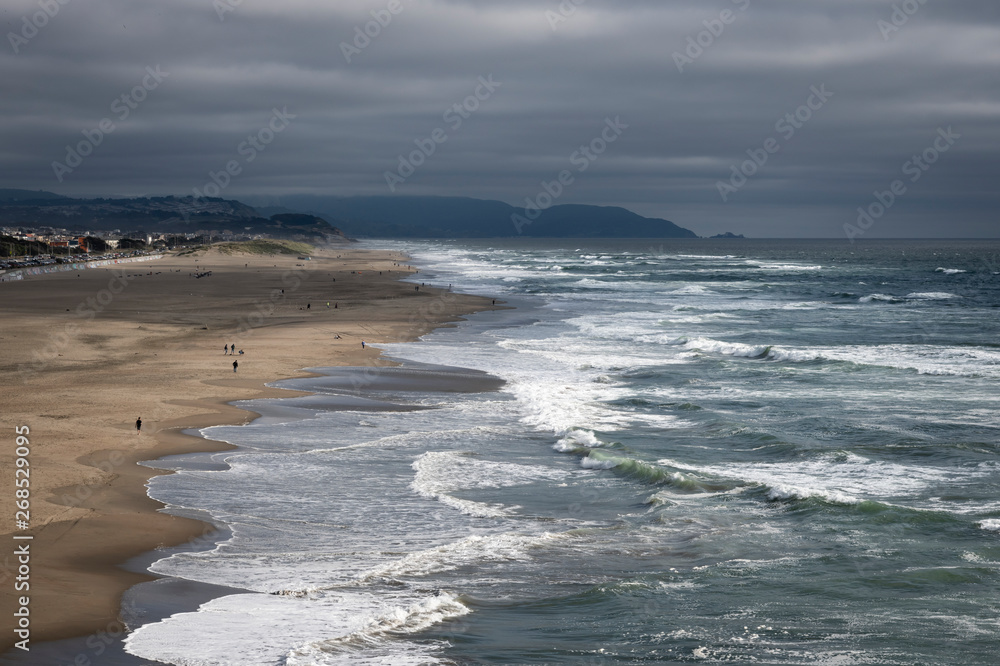 Overcast afternoon at Ocean Beach in San Francisco.  High angle shot looking south from Cliff House.  Mild surf, people enjoying a relatively warm day.