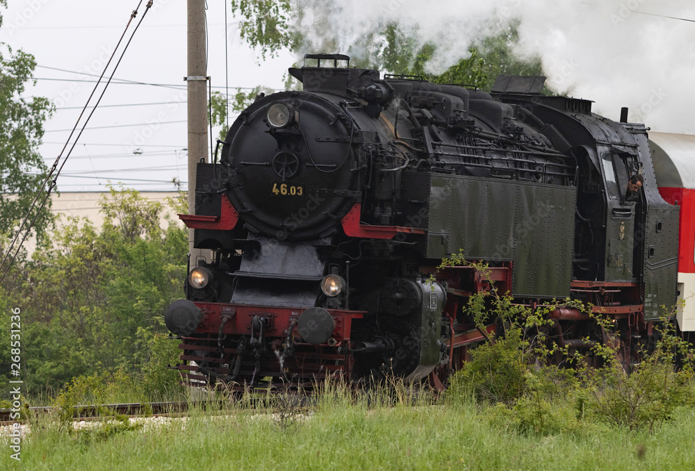 Naklejka premium Historic steam locomotive with passenger wagons speeding on railroad tracks curve and blowing heavy white smoke near Sofia