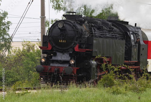 Historic steam locomotive with passenger wagons speeding on railroad tracks curve and blowing heavy white smoke near Sofia