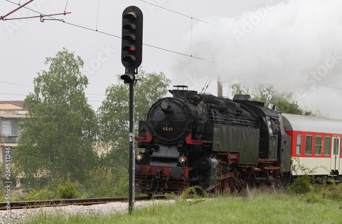 Historic steam locomotive with passenger wagons speeding on railroad tracks curve and blowing heavy white smoke near Sofia