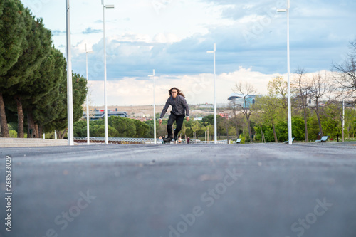 From below young cool male in sportswear riding on roller skates very fast on road in park