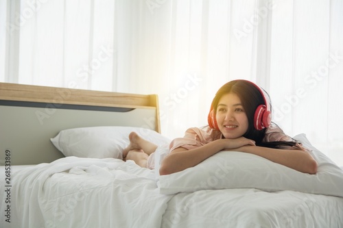 Portait of smiling lady in pink pajama wake up listening to music with headphone welcome morning light on the bed