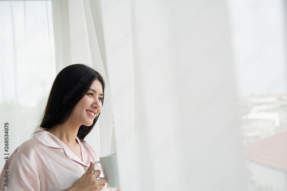 Side view portrait a pretty woman thinking looking holding a coffee mug beside a window with copy space Side view portrait a pretty woman thinking looking holding a coffee mug beside a window with copy space