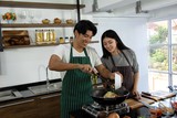 Portrait of cute happy couple in apron in cheerful action  preparing breakfast and adding macaroni and other ingredient decorated with ingredient of food in modern kitche
