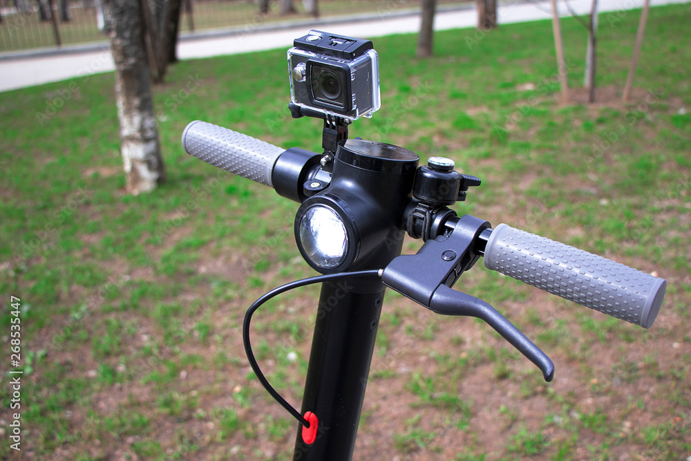 The wheel of the scooter is close-up, an action camera is installed. Electric scooter black with gray handles. The wheel of the scooter is close-up, an action camera is installed. Electric scooter black with gray handles.