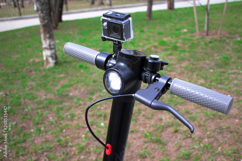 The wheel of the scooter is close-up, an action camera is installed. Electric scooter black with gray handles.