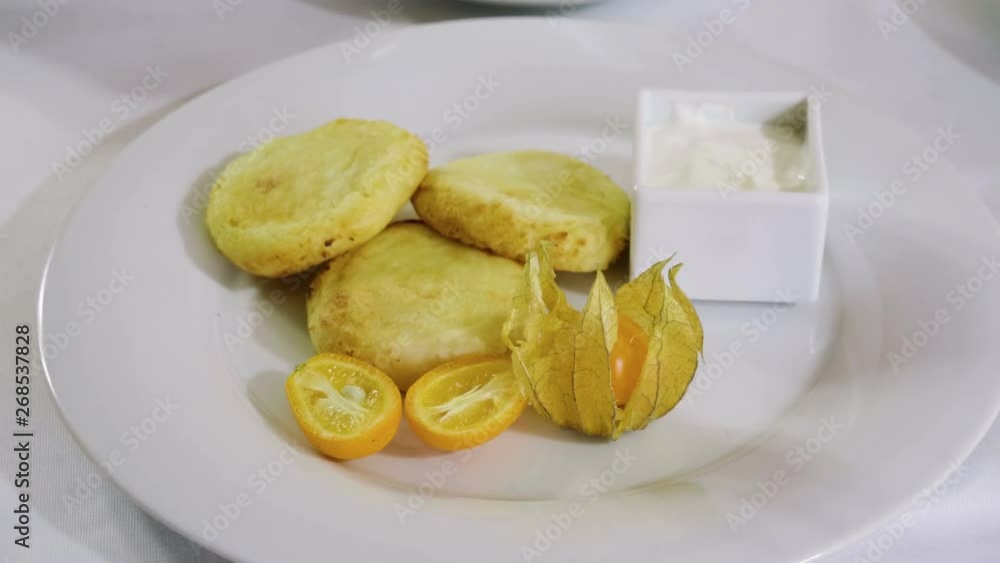 Close-up shot of three cheesecakes, orange, cape gooseberry and sour cream on a white plate. 4K Close-up shot of three cheesecakes, orange, cape gooseberry and sour cream on a white plate. 4K