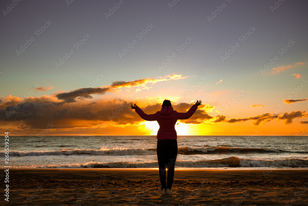 girl standing in a yoga pose at sunset by the sea