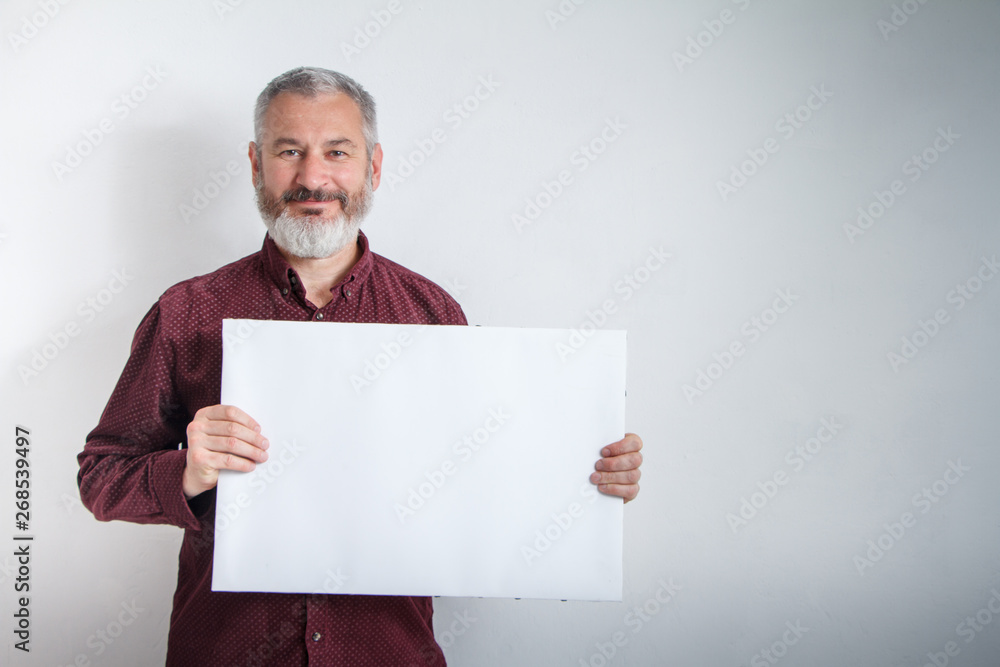 Gray-haired man with a beard holding white empty signboard with space for text in front of him Gray-haired man with a beard holding white empty signboard with space for text in front of him