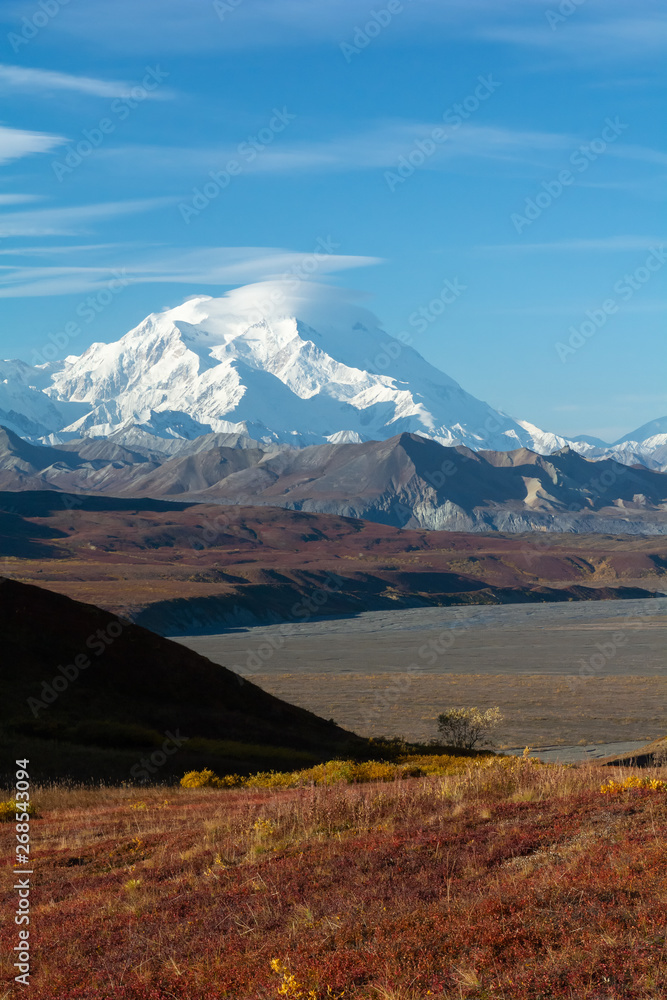 Covered in snow and clouds Mt Denali raises well above gravel foothills