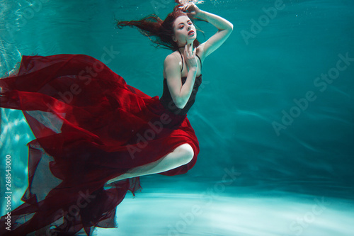 Bild auf Leinwand beautiful young woman in a red dress swims under water
