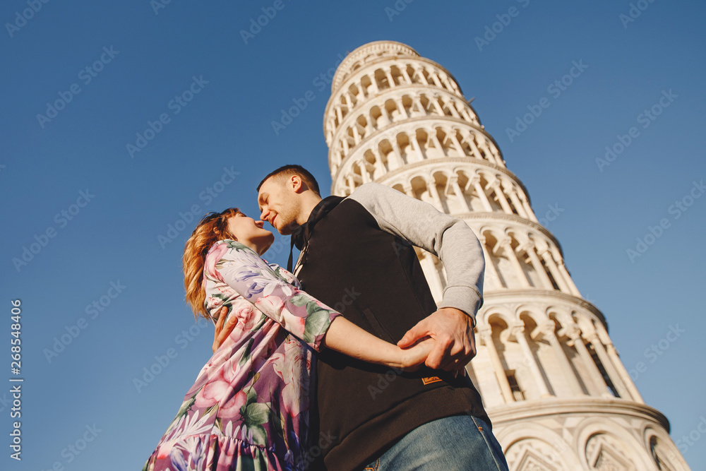 Fototapeta premium Loving couple takes selfie photo on stick and camera against background of leaning Tower Pisa, Italy. Travel concept
