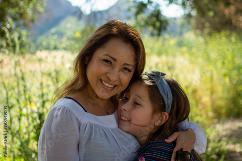 Latina Woman and daughter smiling together in front of a bright field at a park