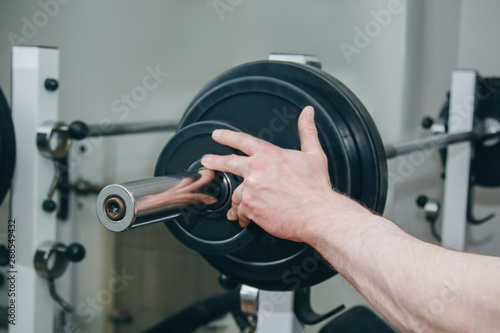 an athlete with big hands adds weight by the metal disks to the training apparatus in the training center. training equipment in the gym close-up