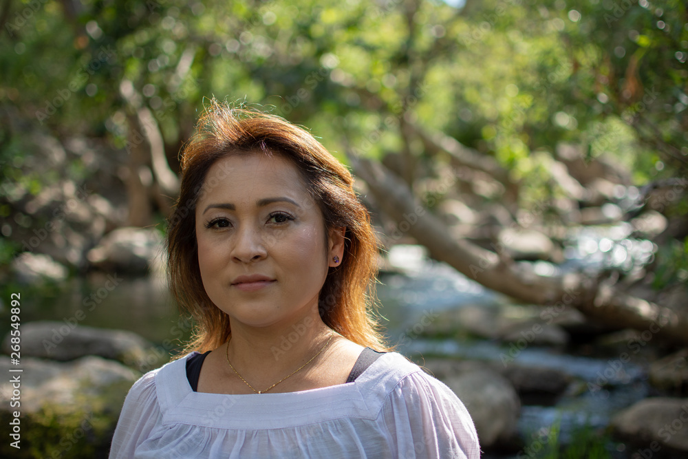 Latina woman with serious expression standing in the shade with glowing hair in a stream with waterfalls in the background