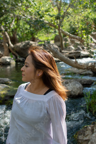 Latina woman with smile standing in the shade with glowing hair in a stream with waterfalls in the background