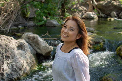 Latina woman with smile standing in the shade with glowing hair in a stream with waterfalls in the background