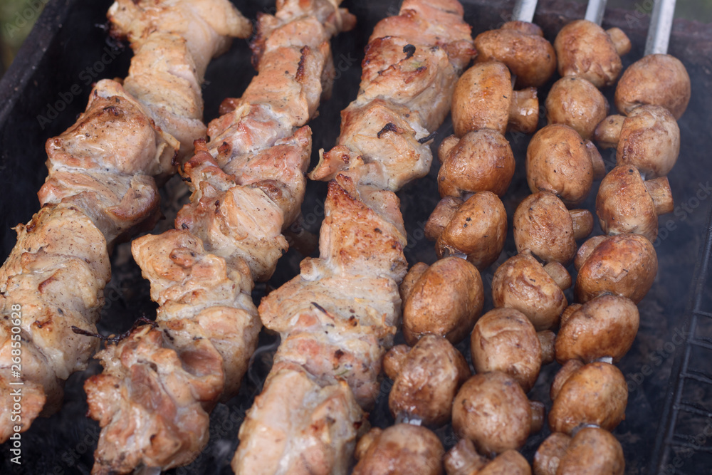 Juicy pieces of meat close-up on the grill on skewers next to delicious mushrooms fried on coals