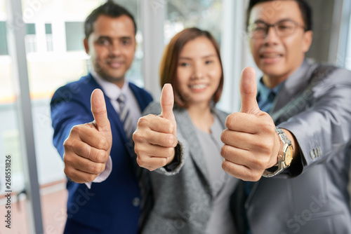 Portrait of group of business people standing together smiling and showing their thumbs up at camera at office