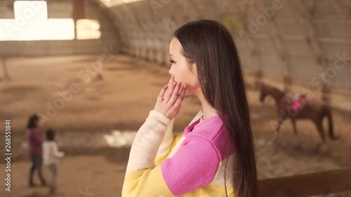 Beautiful woman is standing on a second floor in front of a field where riders on horseback are training with their hourses. photo