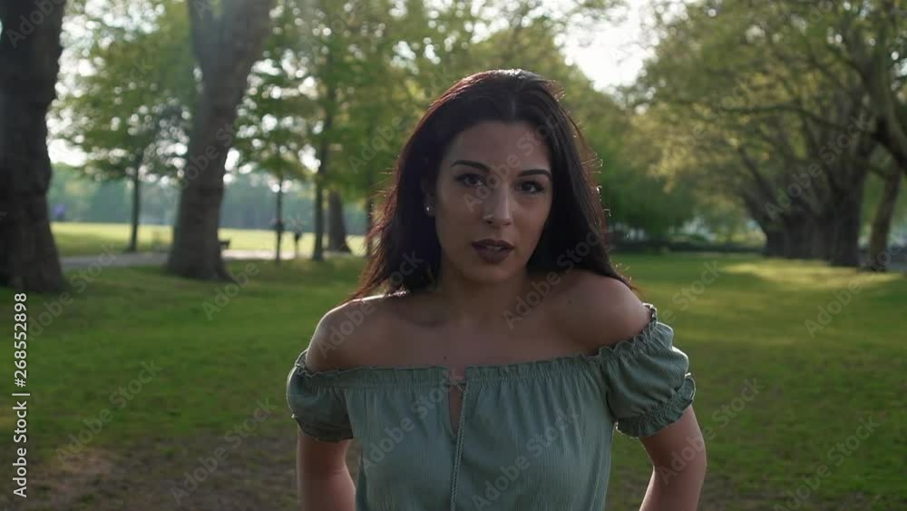 Slow Motion Portrait of a gorgeous hispanic latino young woman looking at the camera, blinking and flirting, with a beautiful British park in the background. Slow Motion Portrait of a gorgeous hispanic latino young woman looking at the camera, blinking and flirting, with a beautiful British park in the background.