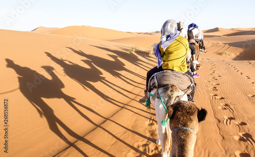 Tourists caravan riding dromedaries through sand dunes in Sahara desert near Merzuga in Morocco - Wanderlust travel concept with people travelers on camel trip adventure tour - Warm bright filter photo