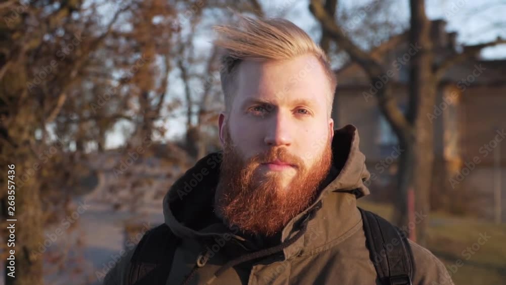 Close up portrait serious handsome full bearded Caucasian male looking fearless into the camera. Confident stylish man with a beard. Windy outdoors scenery. Handheld horizontal slow motion footage. Close up portrait serious handsome full bearded Caucasian male looking fearless into the camera. Confident stylish man with a beard. Windy outdoors scenery. Handheld horizontal slow motion footage.