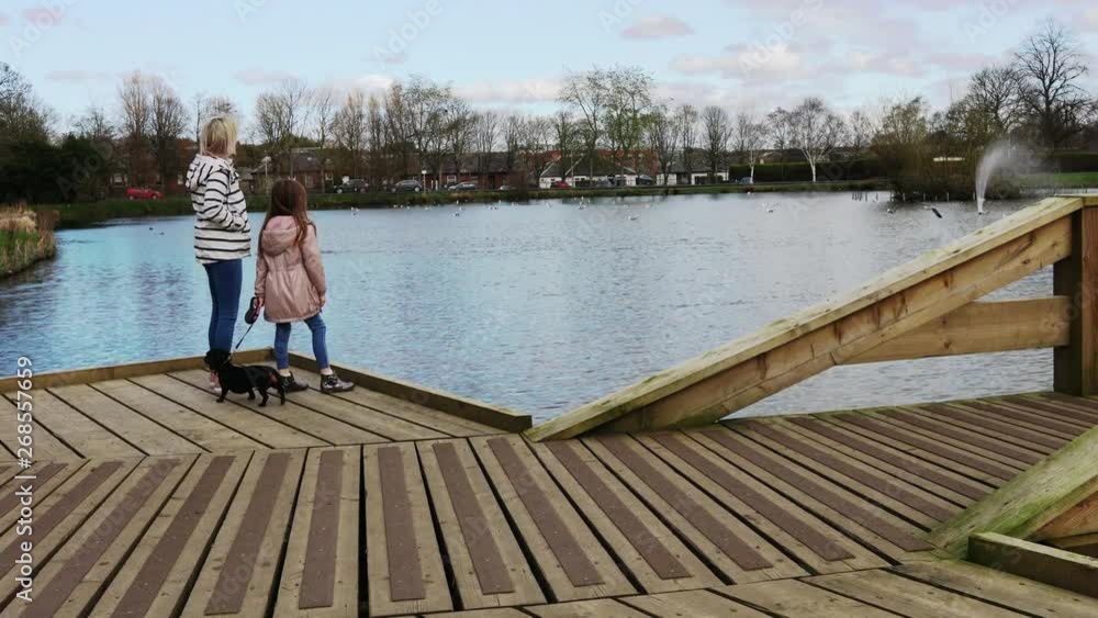 A young Mum, her daughter and their dog look out onto the local pond A young Mum, her daughter and their dog look out onto the local pond