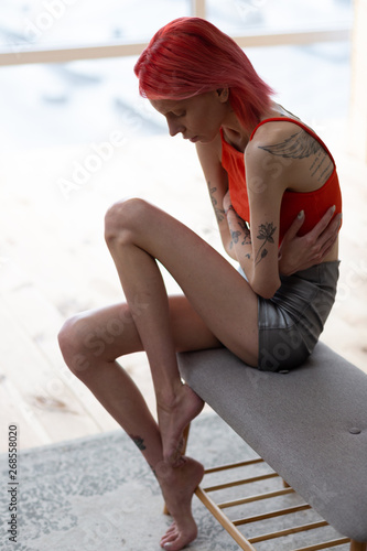 Red-haired anorexic woman with tattoos having pain in stomach photo