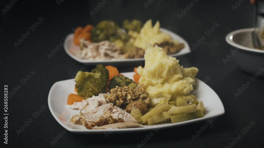 Dinner plates filled with roasted chicken, mashed potatoes, leeks and other delicious steaming hot food. Spooning side dishes onto plates before serving a meal.