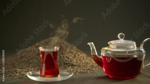 Hot tea beside the teapot. Tea leaves at the background
