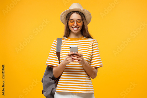 Positive Caucasian girl isolated on yellow background browsing pages in her smartphone ready to travel