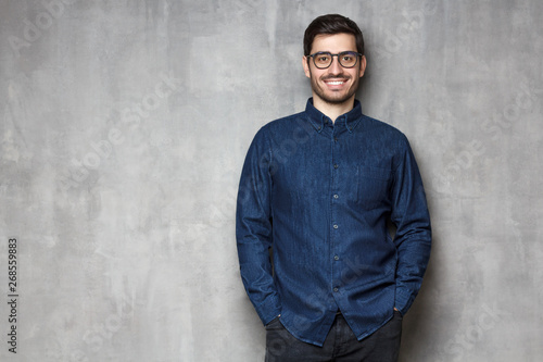Young handsome male smiling and feeling confident, standing against textured wall background, copy space on left