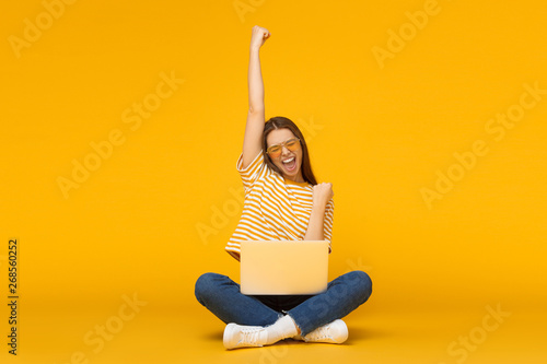 She is a winner! Excited young female with laptop isolated on yellow background