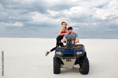 a girl climbs her boyfriend on a quad bike, they are preparing for a trip in the desert, a stylish young couple