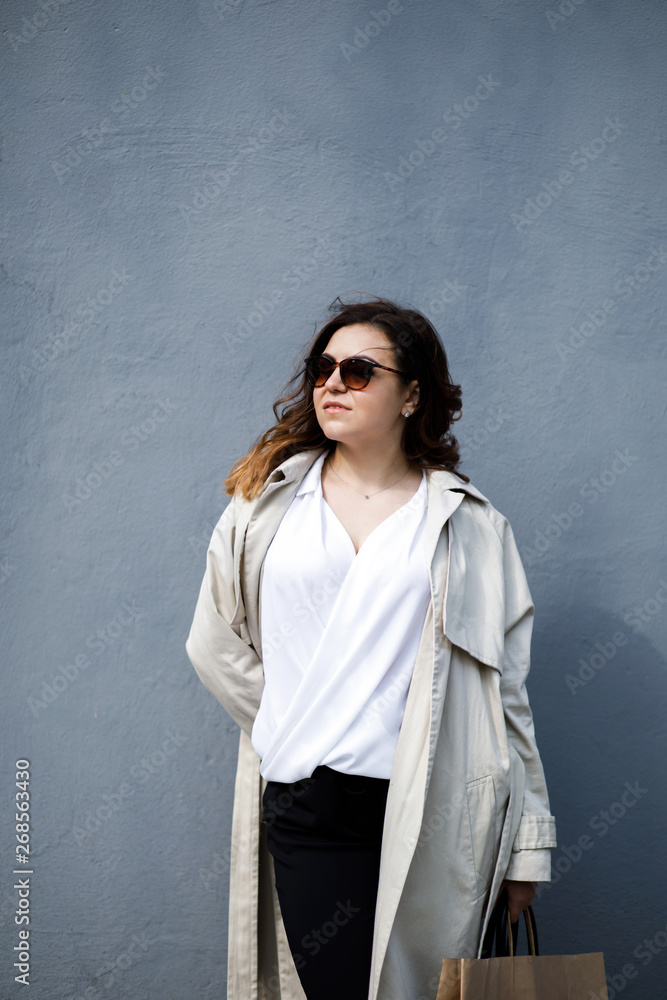 A young, sympathetic woman, not a thin-headed body building, stands on the background of the wall. Business clothing style. A young, sympathetic woman, not a thin-headed body building, stands on the background of the wall. Business clothing style.