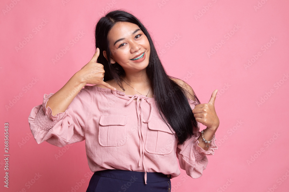 Young Asian woman thumbs up show with phone gesture. Young Asian woman thumbs up show with phone gesture.