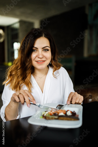 A young  sympathetic woman  not a thin-headed body building  sits in a cozy cafe and eats a salad. Business clothing style.