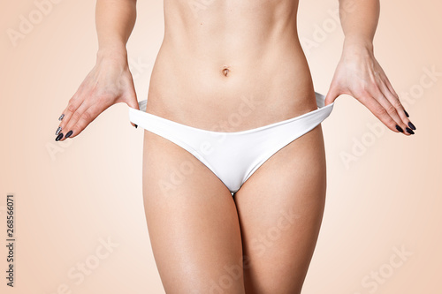 Studio short of bautiful halthy fmale's body. Smooth soft skin, lady touching her white panties with thumbs. Slim girl with perfect body shape, flat belly in underwear. Health, hygiene concepts.
