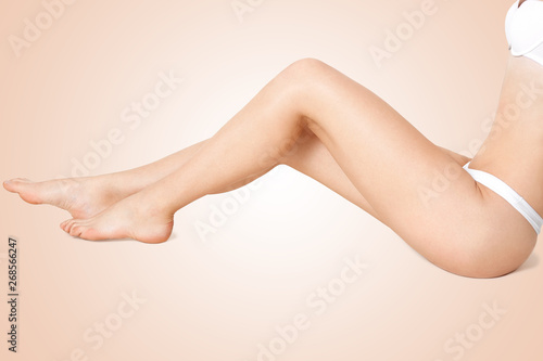 Faceless portrait of woman's leg, female sitting down in studio wearing white lingerie, showing her perfect silky skin, demonstrating ideal depilation. Skin care, body care and hygiene concept.