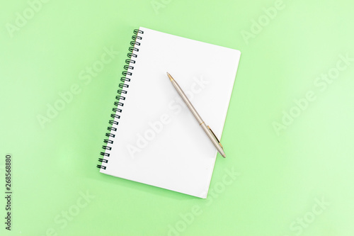 White notepad with steel pen on a green background. Office table, minimal composition. Copy space.