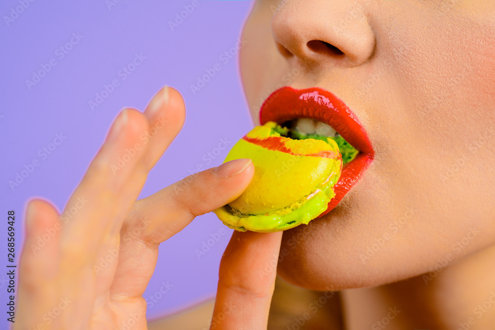 Young woman eating french macaroon. Closeup. Beautiful fashion model girl with red lips taking colorful macaroons. Female holds colorful macaroon. French dessert. Sweets. Beautiful woman bite macaroon Young woman eating french macaroon. Closeup. Beautiful fashion model girl with red lips taking colorful macaroons. Female holds colorful macaroon. French dessert. Sweets. Beautiful woman bite macaroon
