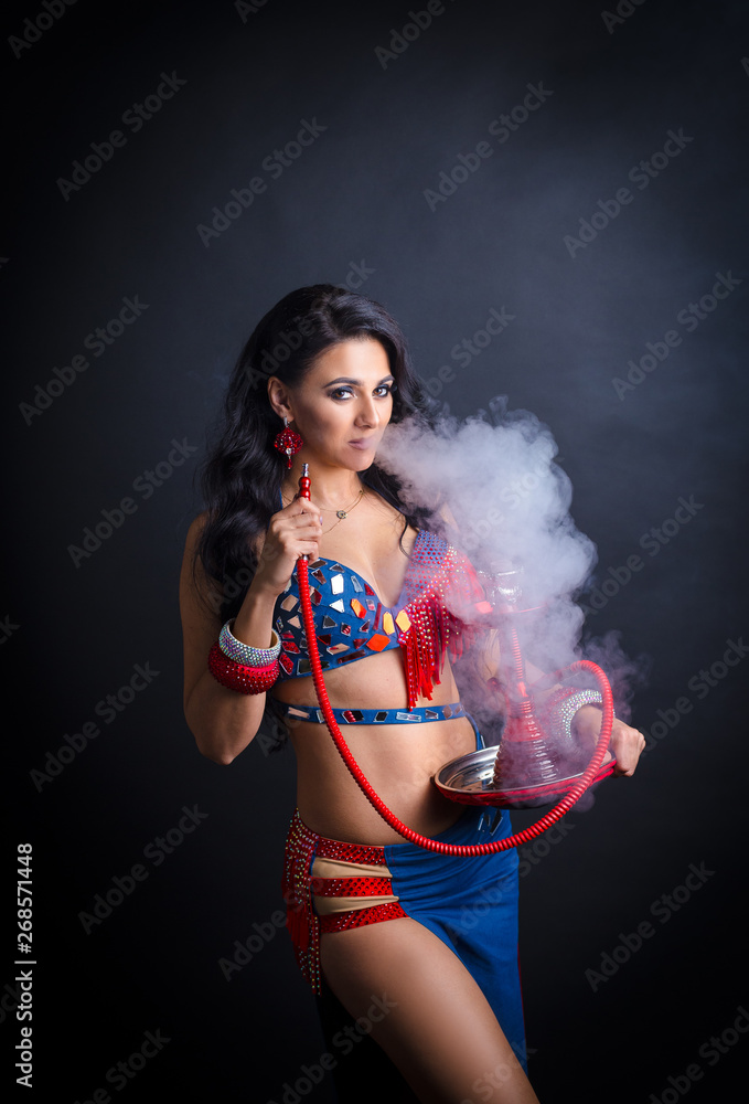 Portrait of a beautiful oriental girl in a sexy costume. girl smokes a hookah and exhales smoke