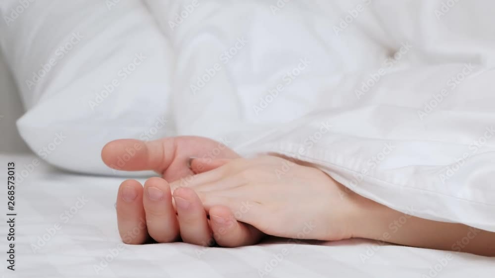 The hands of the couple, men and women stick out from under the blanket. Fingers are woven. Tenderness and love. Sleep together. The hands of the couple, men and women stick out from under the blanket. Fingers are woven. Tenderness and love. Sleep together.