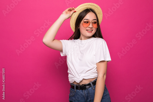 Pleased asian young woman in straw hat and sunglasses posing over pink background © F8  \ Suport Ukraine