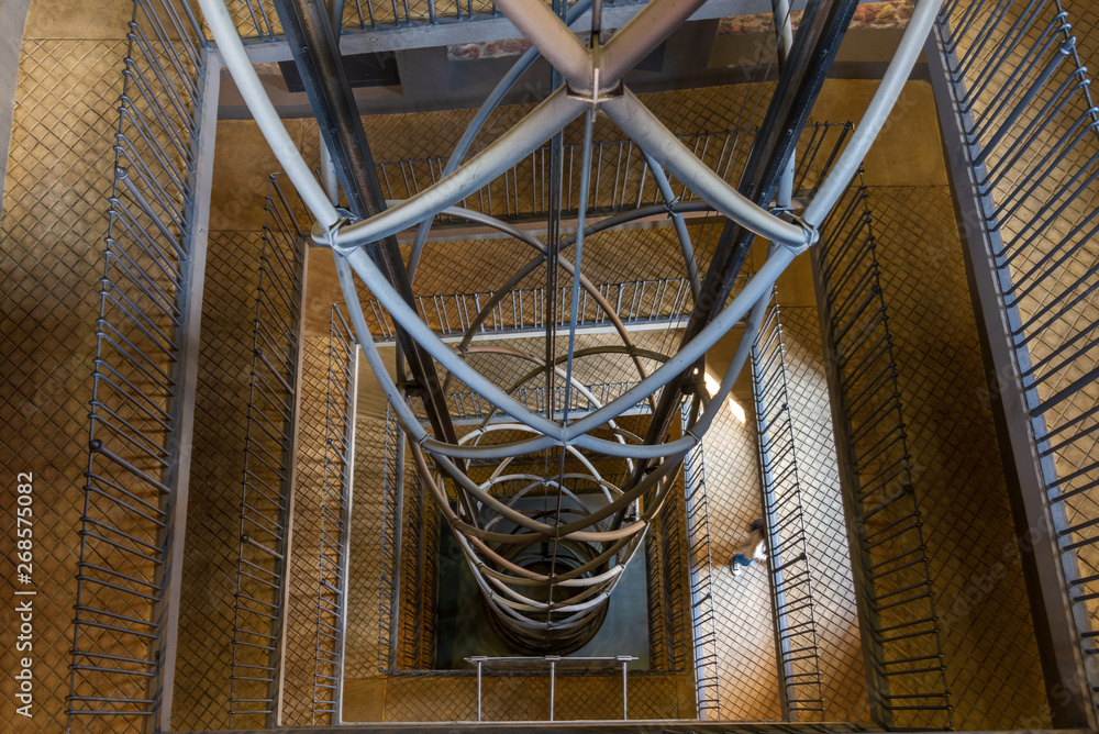 Obraz premium Diminishing perspective low angle view of staircase with square stair hall in the middle and open elevator wrapped with twist iron structure in Astronomical Clock Tower in Prague, Czech Republic.