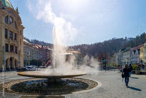 Outdoor sunny view at steam of water gush raise to the air at fountain of hot mineral thermal spring in front of Hot Spring Colonnade in Karlovy Vary, Czech Republic..