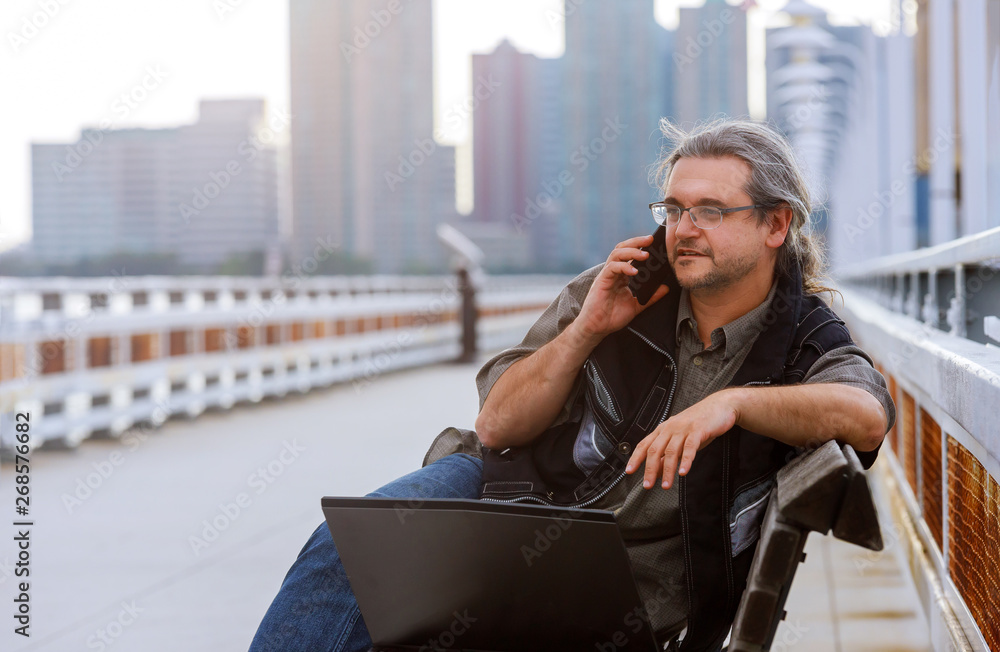 Businessman sitting on the with New York cityscape with smart phone in outdoor.
